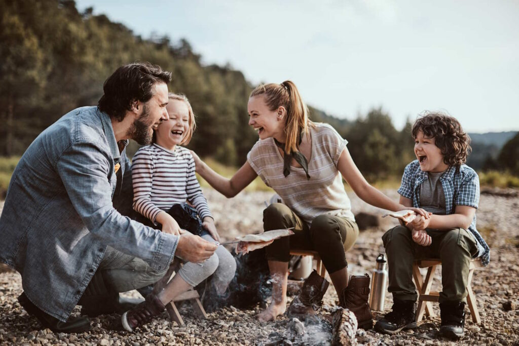 Familie mit Kindern macht Lagerfeuer am Flussbett.